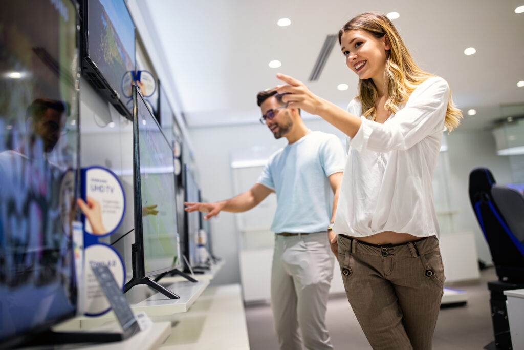 Young couple in consumer electronics store looking at latest digital devices, television. 