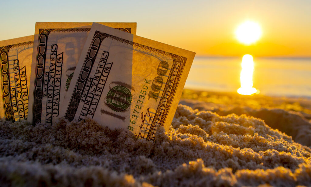 Three dollar bills are buried in sand on sandy beach near sea at sunset dawn in summer heat close-up. Money. Dollars covered sand. Money grows in ground. Finance and investment concept.